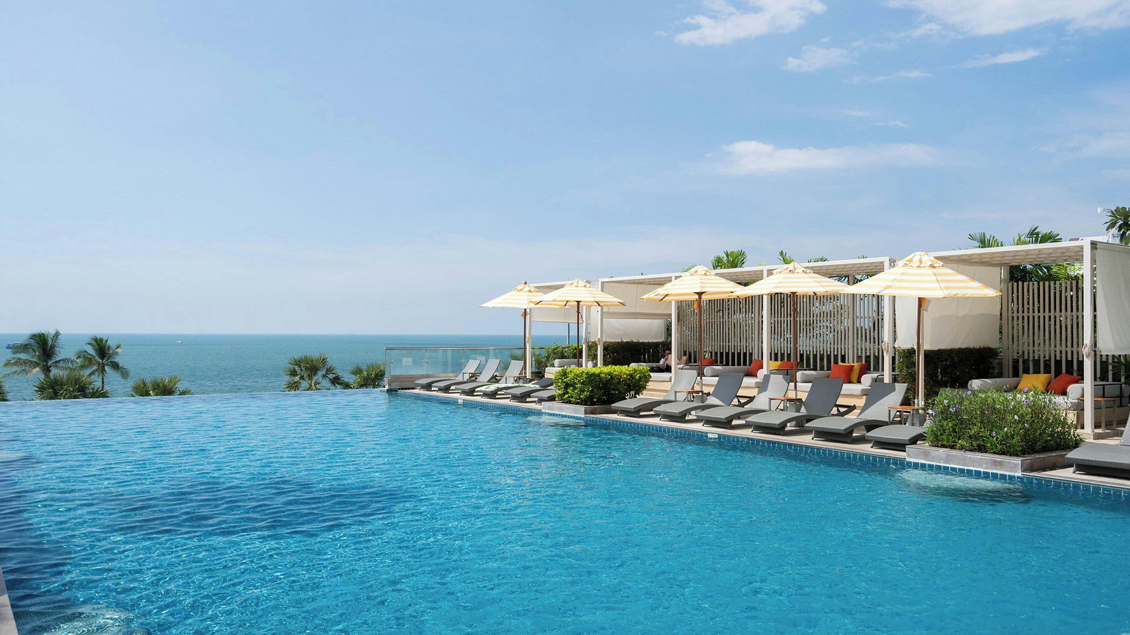 A swimming pool with lounge chairs and umbrellas, overlooking the sea.