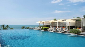 Piscina con sillones de playa y sombrillas, con vista al mar.