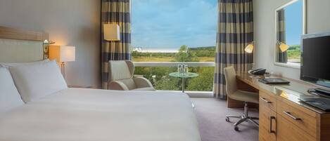 A hotel room with a large bed, a desk with a computer, a chair, and a view of the outdoors through a window.