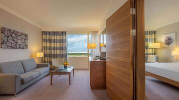 A hotel room with a sofa, a desk, a bed, a view of the outdoors, and a wooden partition.