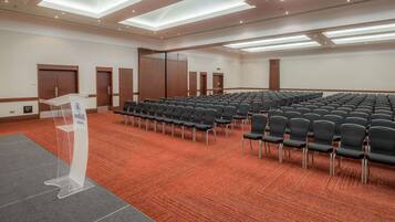 A conference room with rows of black chairs, a podium, and wooden doors.