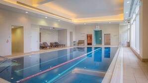 Una amplia piscina interior con separadores de carril, sillones de descanso aledaños y un diseño de interiores moderno.
