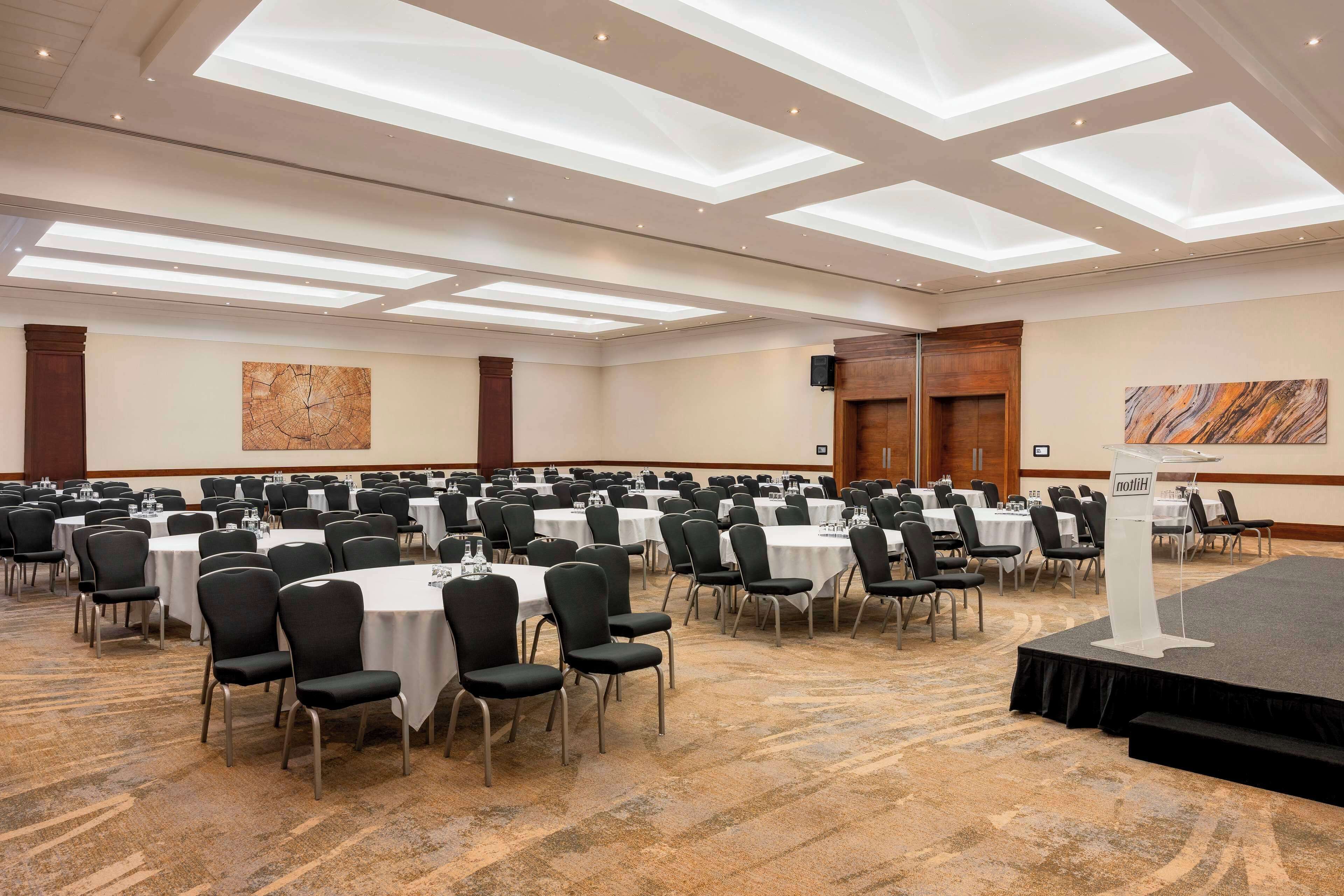 A conference room with multiple tables and chairs, a stage with a podium, and artwork on the walls.