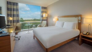 Habitación de hotel con una cama grande, un escritorio con computadora, una silla y vistas al exterior.