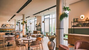 Un café espacioso con mobiliario de madera, plantas colgantes y grandes ventanales.