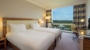 A hotel room with two beds, a desk with a chair, a TV, and a view of the outdoors.