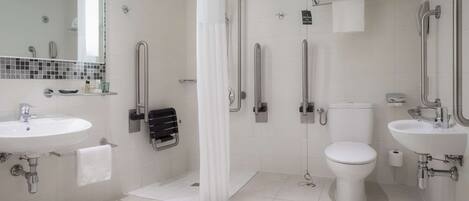 A modern bathroom with a shower, toilet, and two sinks, equipped with grab bars and a scale.