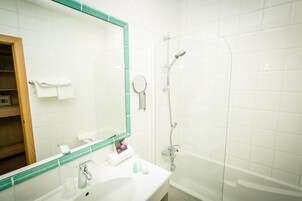 A bathroom with a white sink, a mirror with a green frame, a shower, and a white tiled wall.