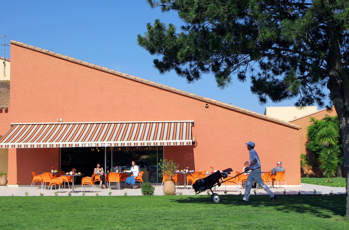 Un espace extérieur aménagé avec des chaises orange et un auvent rayé.