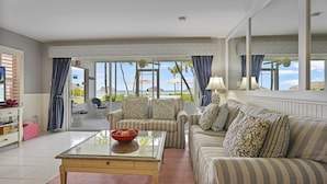 A living room with a glass coffee table, striped sofas, and a view of the beach. - Aqua Bay Club Condos (Seven Mile Beach)