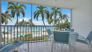 A balcony with a view of a pool and palm trees, a table with chairs, and a starfish decoration. - Aqua Bay Club Condos (Seven Mile Beach)