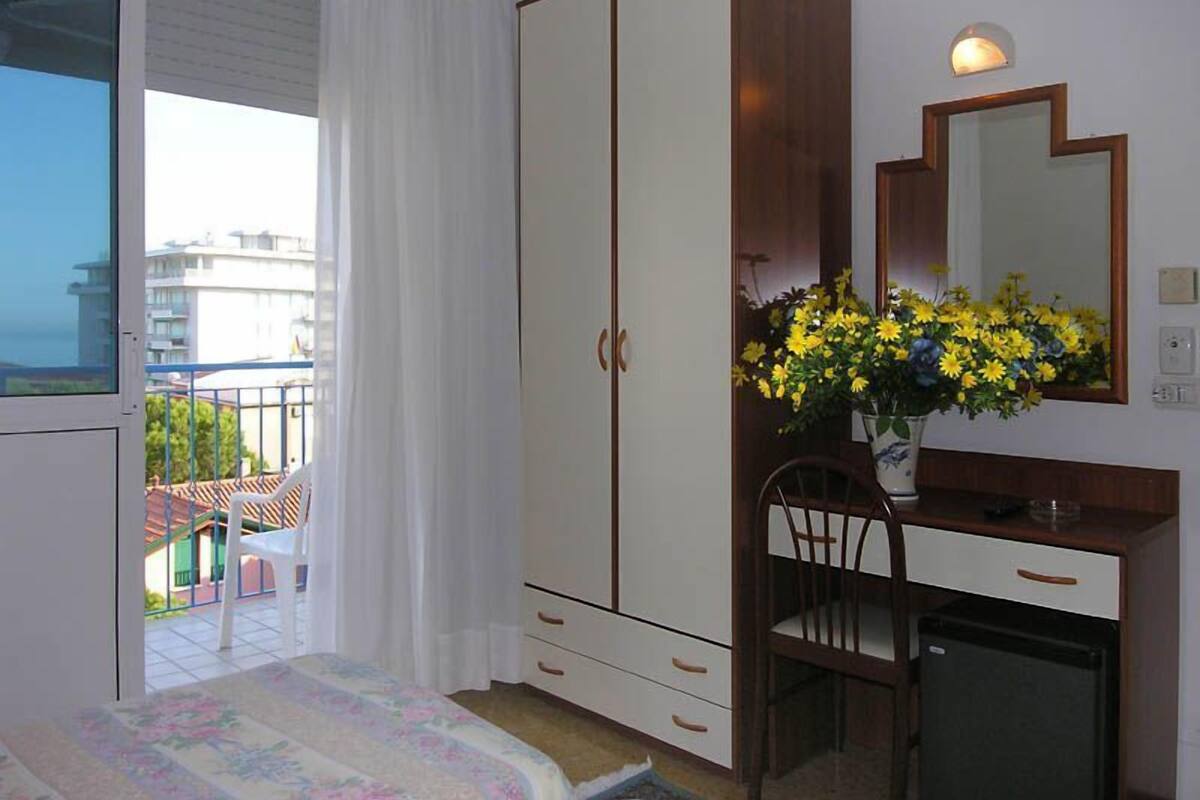 A bedroom with a bed, a wardrobe, a desk, a chair, and a mirror.