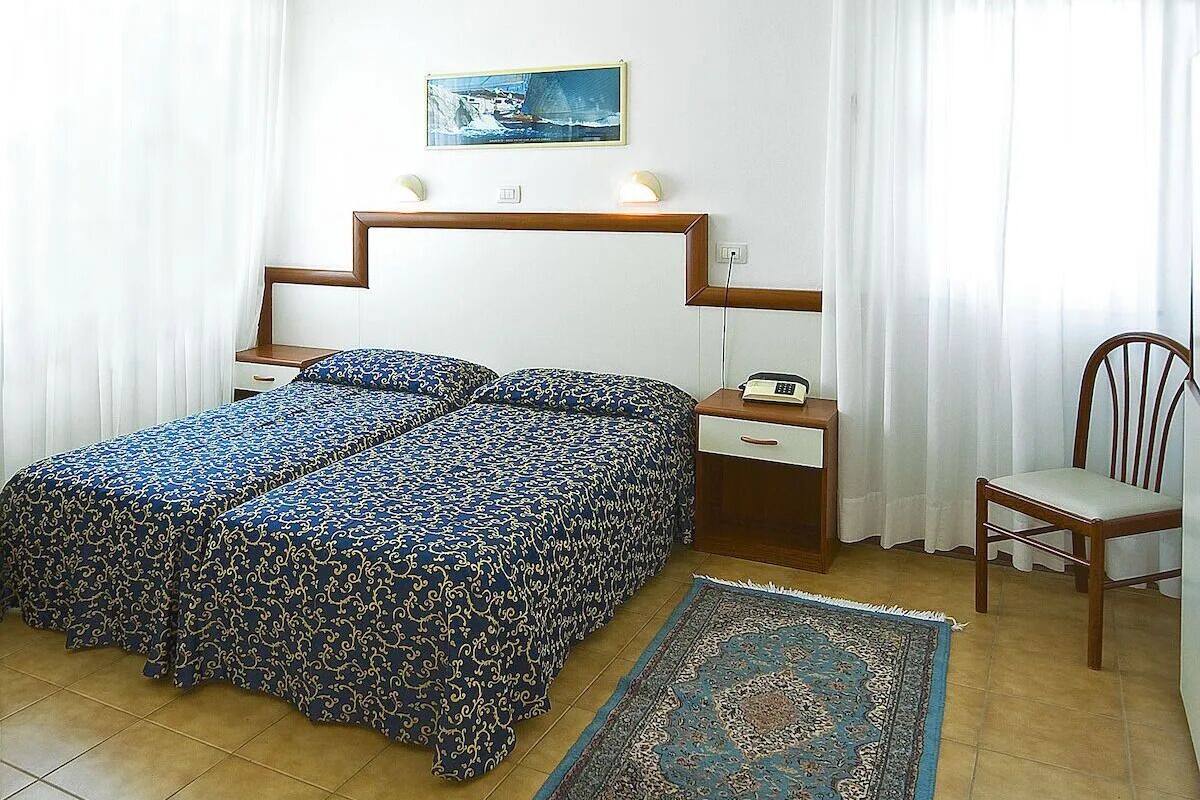 A bedroom with a bed, bedside table, chair, and a rug.
