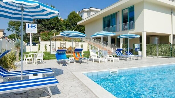 Zona de piscina de hotel con sombrillas a rayas azules, sillones de descanso y un cartel que indica 'HB' y 'Boulevard'.