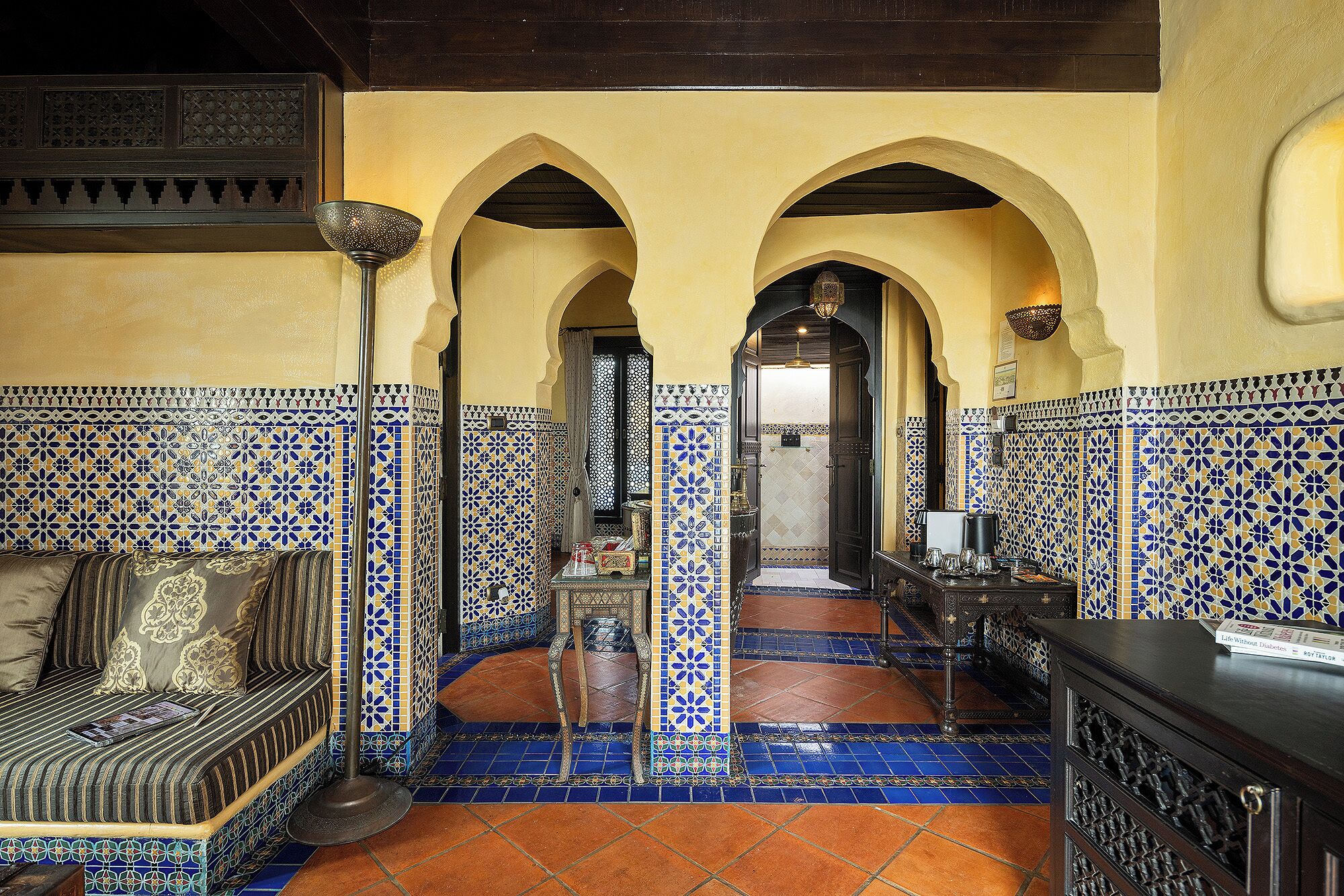 Un interior marroquí tradicional con una pared de azulejos decorados, un sofá con cojines, una mesa de centro y un suelo de azulejos.