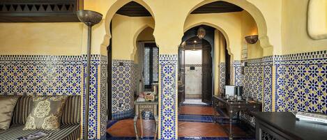 Un interior marroquí tradicional con una pared de azulejos decorados, un sofá con cojines, una mesa de centro y un suelo de azulejos.