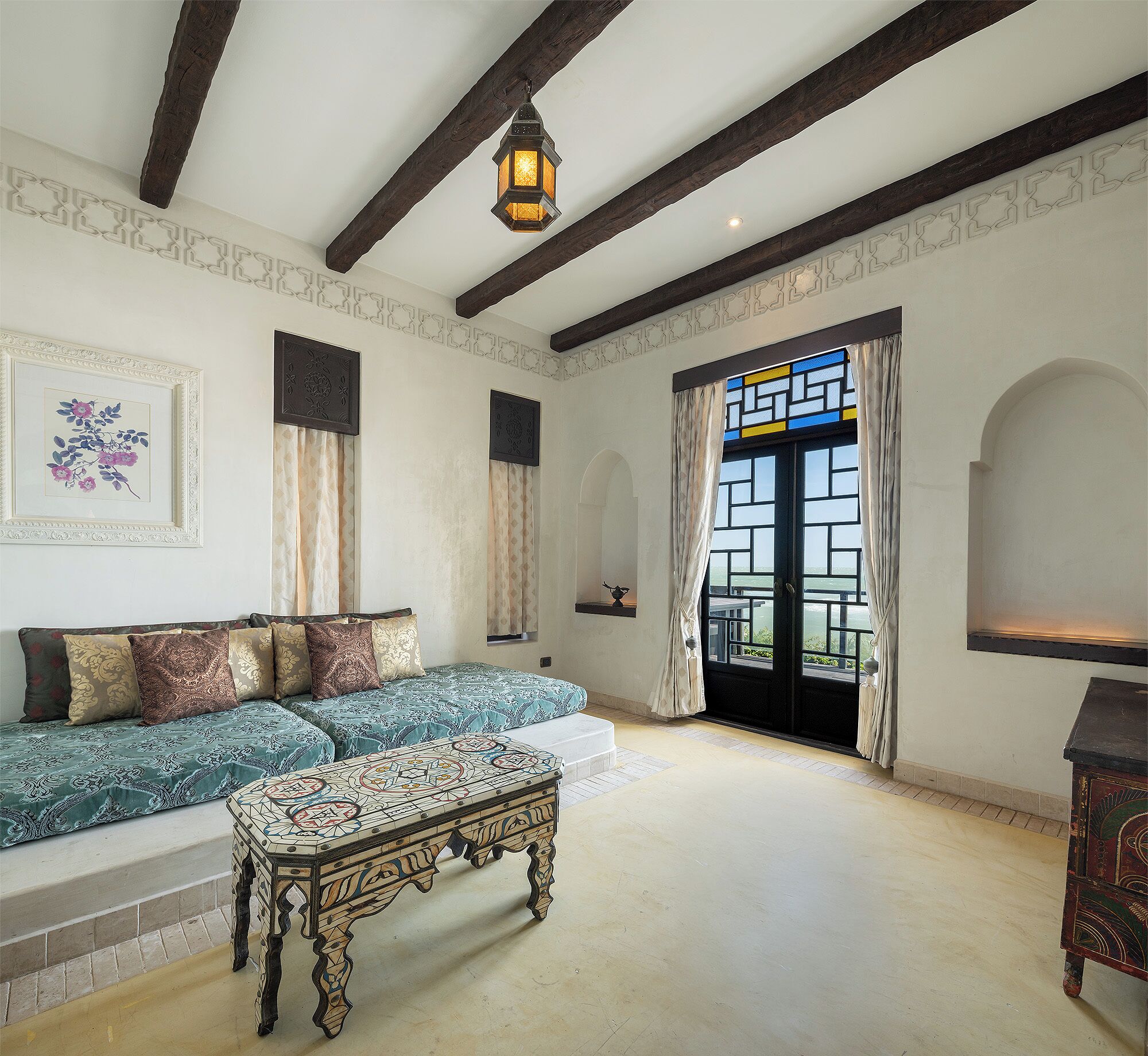 A room with a sofa, a patterned ottoman, a wooden cabinet, and a hanging lantern.
