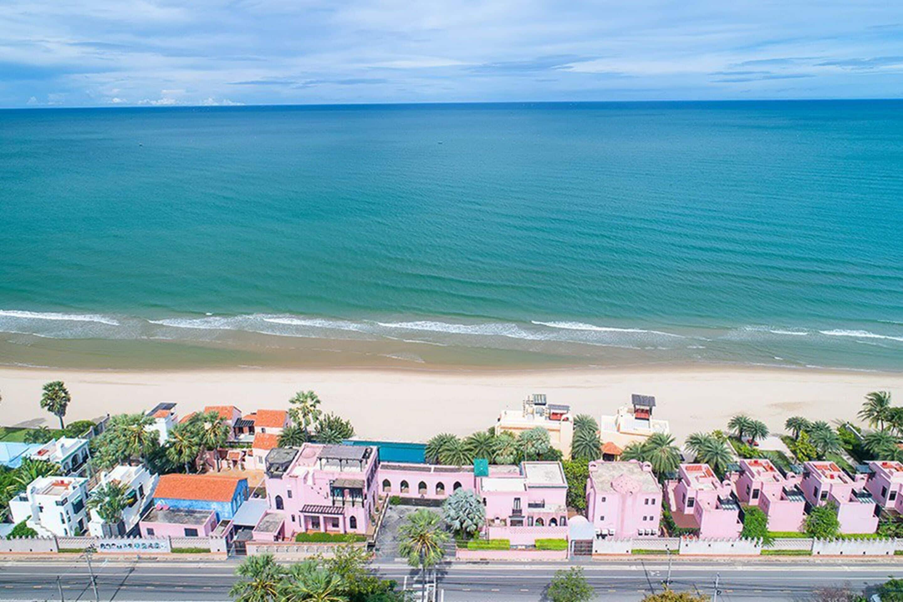 Une ville côtière avec des bâtiments qui bordent la plage, une vue dégagée sur l’océan et une route qui mène au rivage.