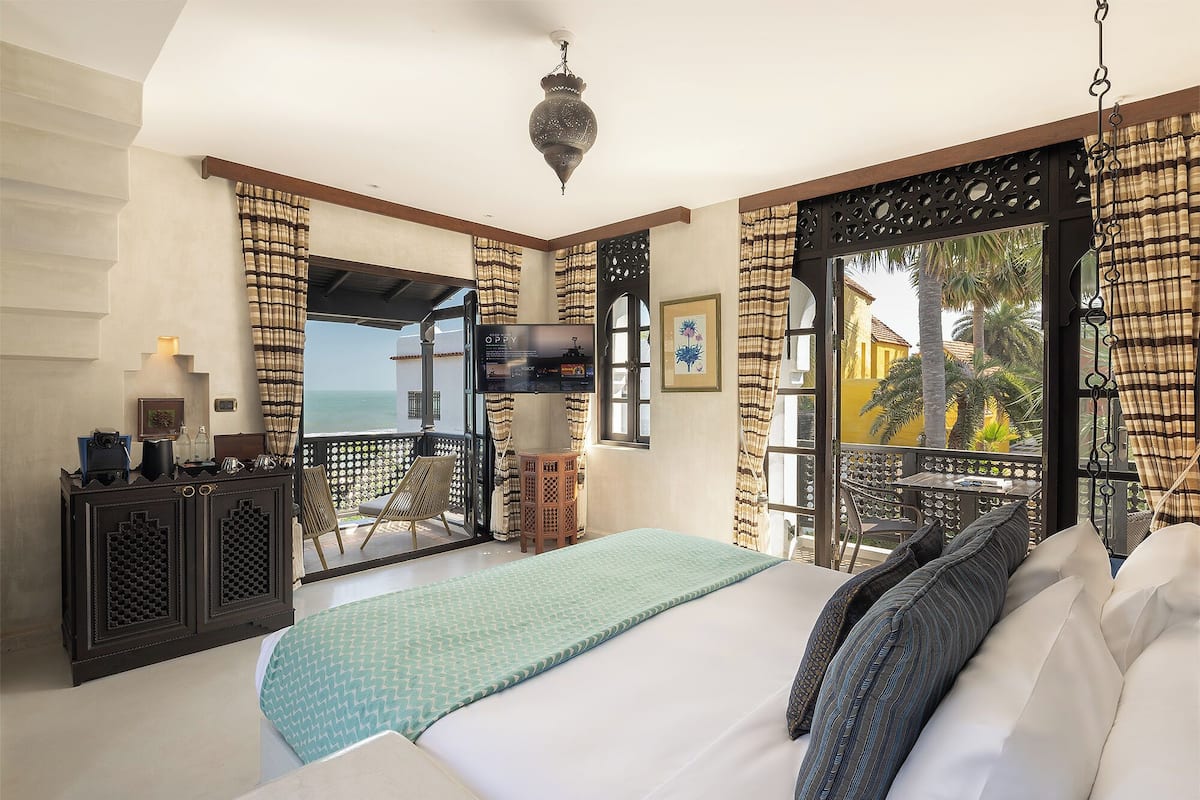 A bedroom with a bed, a TV, a balcony with a view of the sea, and a decorative hanging light.