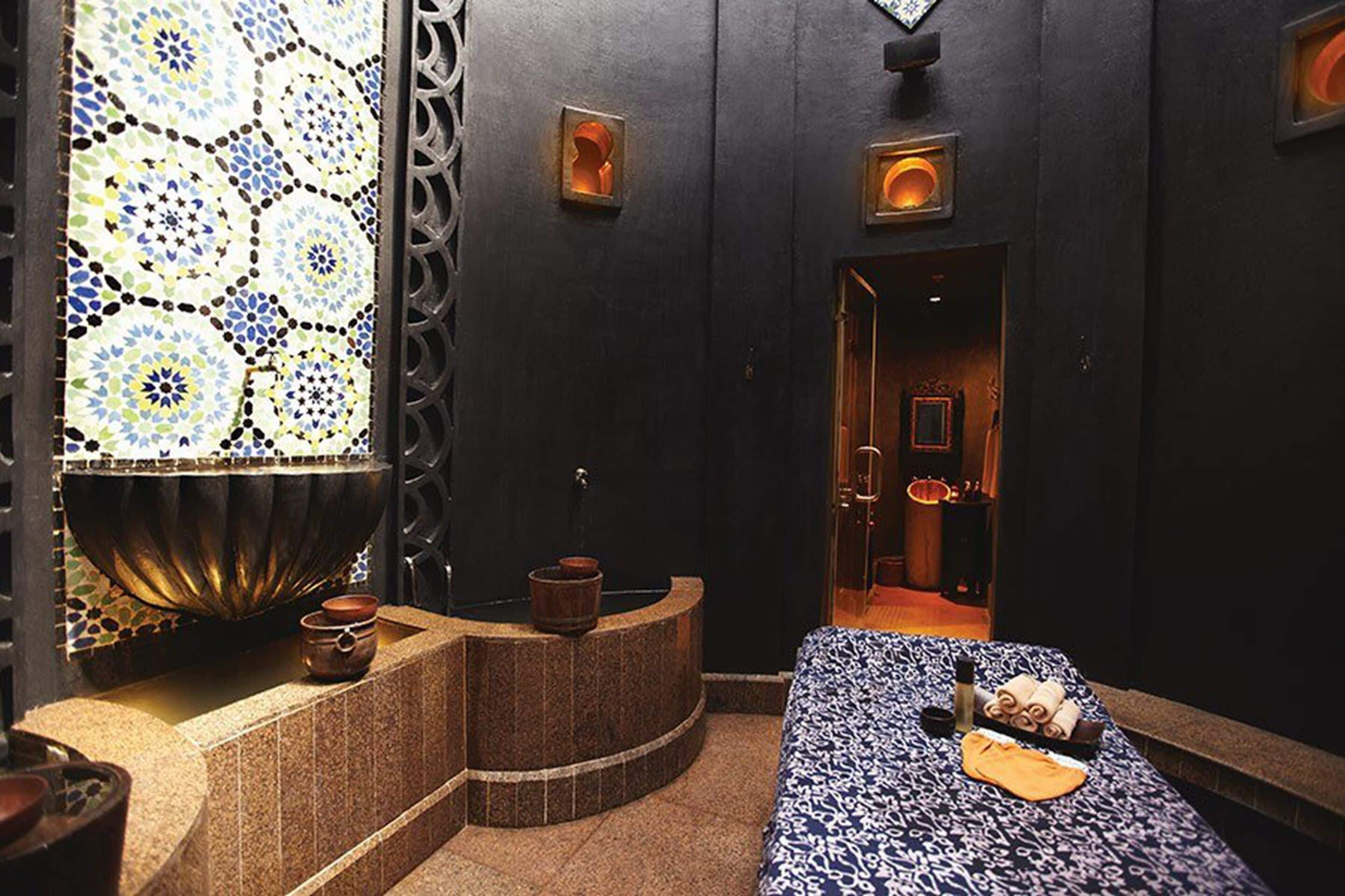 A spa room with a bed, a small seating area, and a decorative wall with a mosaic pattern.