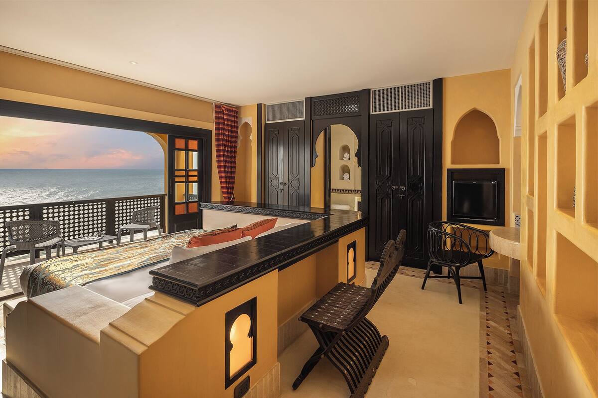 A balcony with a view of the ocean, a seating area with a bench, and a bar counter.