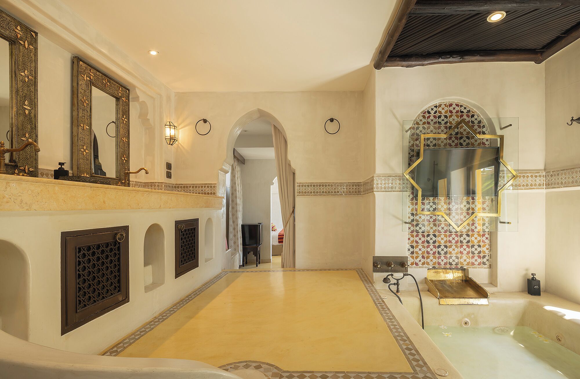 A spacious bathroom with a large bathtub, a mirror with decorative frame, and a tiled wall.