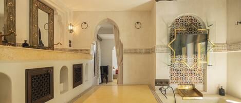 A spacious bathroom with a large bathtub, a mirror with decorative frame, and a tiled wall.