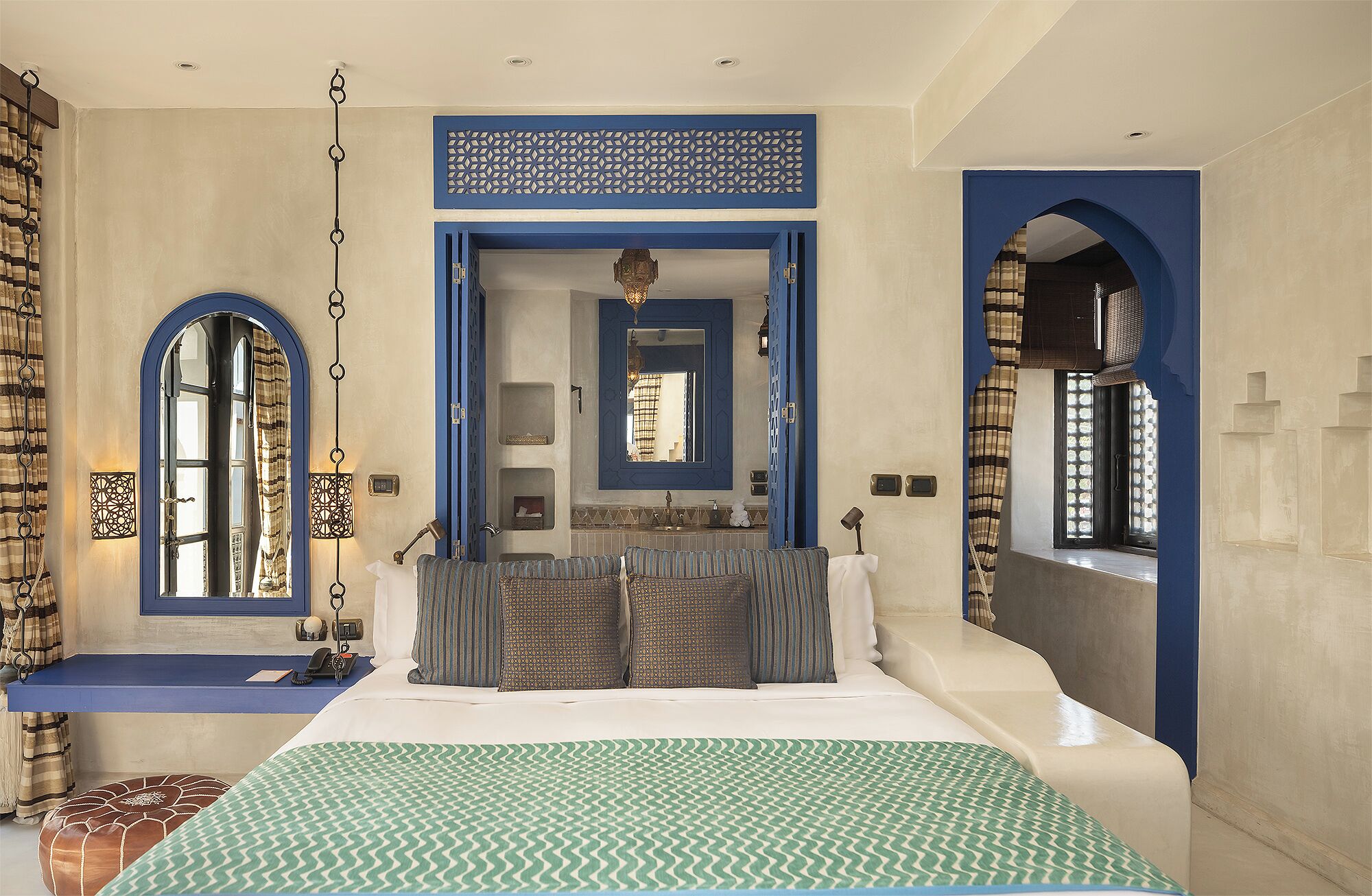 A bedroom with a large bed, a bathroom with a mirror, and a view through an archway.