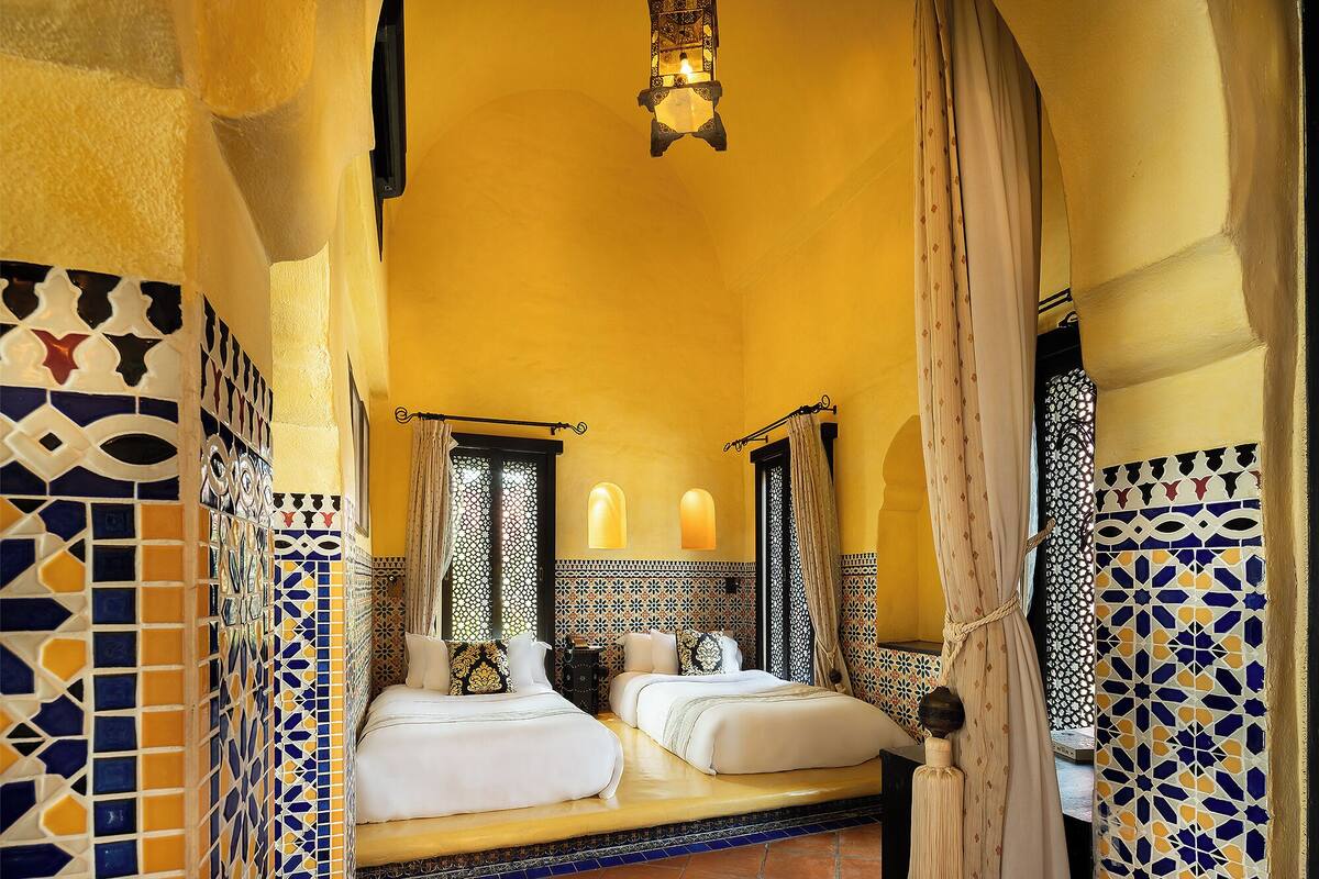 A room with two beds, patterned walls, and a hanging light fixture.