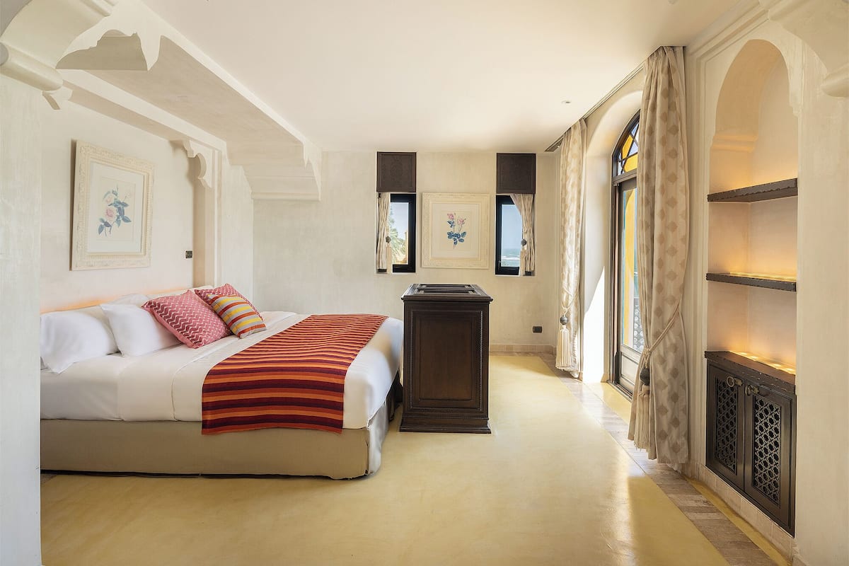 A bedroom with a bed, a nightstand, a dresser, and a window with curtains.
