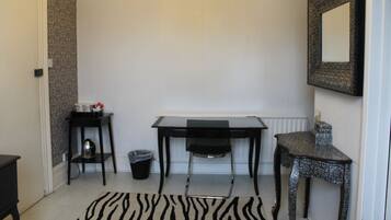 Quarto pequeno e limpo, com escrivaninha, cadeira e um tapete com padrão de zebra.