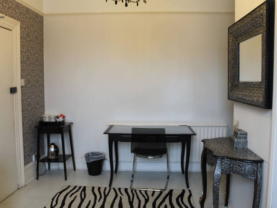 Quarto pequeno e limpo, com escrivaninha, cadeira e um tapete com padrão de zebra.