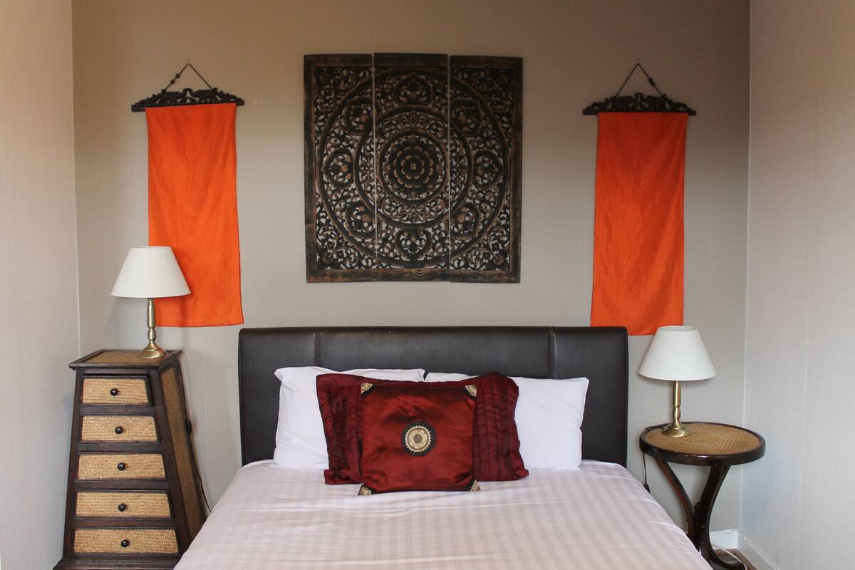 A neatly made bed with white linens, a dark headboard, and a red decorative pillow. There are two bedside tables, each with a lamp and a small round table.