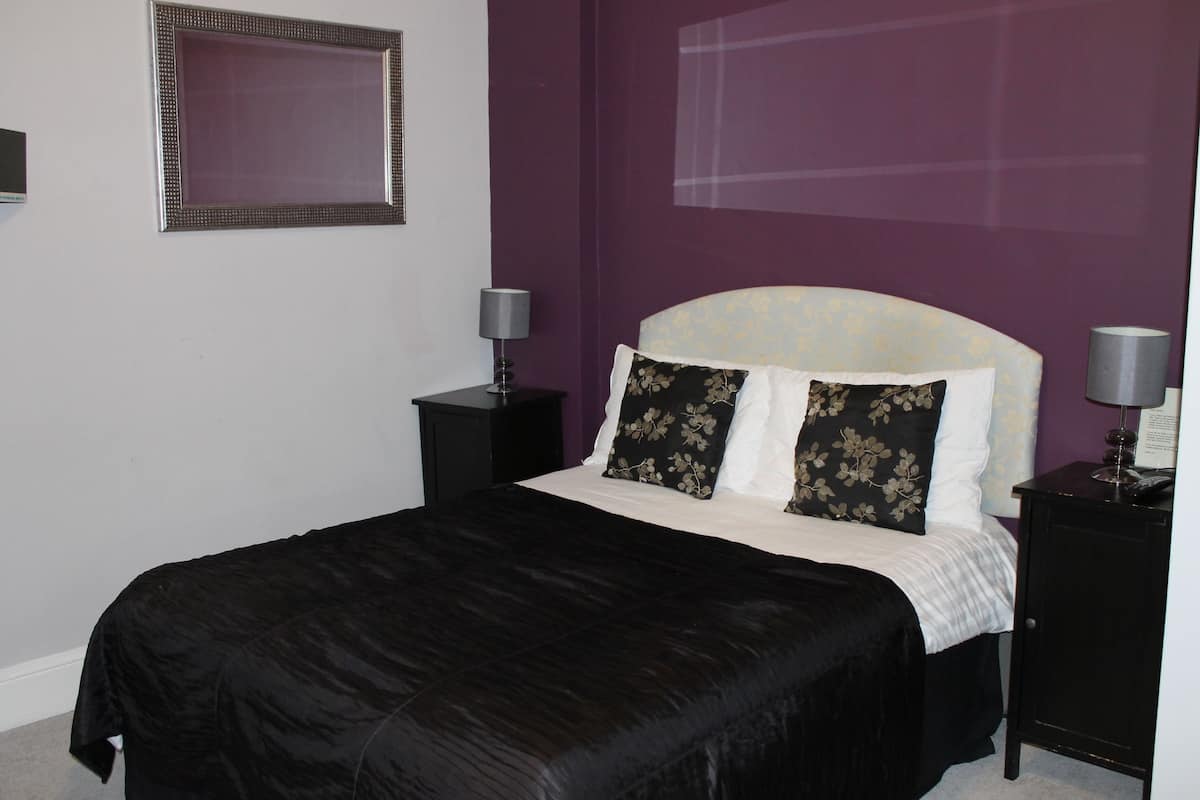 A neatly made bed with a black bedspread, two nightstands with lamps, and a framed mirror on the wall.