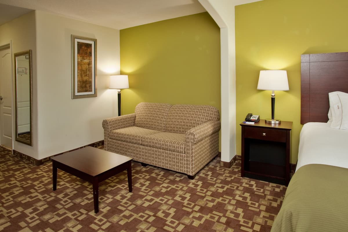 A hotel room with a patterned sofa, a small table, a bed, and two bedside lamps.