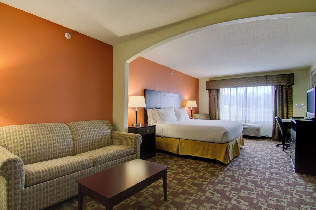 A hotel room with a bed, a sofa, a coffee table, and a desk with a chair.