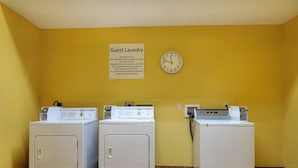 A laundry area with three washers and dryers, a clock, and a sign indicating guest laundry use only.