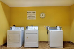 A laundry area with three washers and dryers, a clock, and a sign indicating guest laundry use only. - Holiday Inn Express Hotel & Stes Kansas City Sports Complex by IHG (Kansas City)