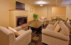 A hotel room with a fireplace, patterned sofas, a coffee table, and a dining area with chairs and a table. - Holiday Inn Express Hotel & Stes Kansas City Sports Complex by IHG (Kansas City)