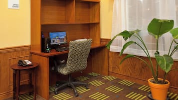 A hotel office center with a desk, computer, chair, telephone, and a potted plant.