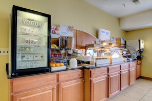 A breakfast buffet area with a refrigerated display of yogurt and milk, cereal options, and a variety of fruits. - Holiday Inn Express Hotel & Stes Kansas City Sports Complex by IHG (Kansas City)