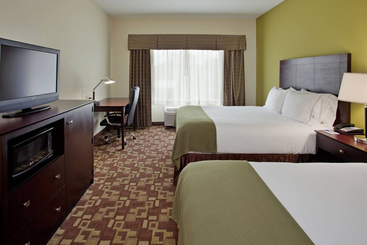 A hotel room with a bed, a desk with a television, a chair, and a lamp.