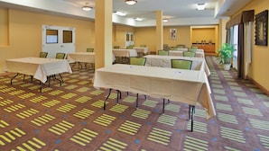 A hotel conference room with multiple tables and chairs, a reception desk, and a large window with curtains.