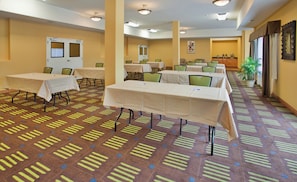 A hotel conference room with multiple tables and chairs, a reception desk, and a large window with curtains. - Holiday Inn Express Hotel & Stes Kansas City Sports Complex by IHG (Kansas City)