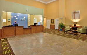 A hotel reception area with a wooden reception desk, a digital clock, and a seating area with a green sofa and a coffee table.