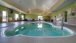 An indoor swimming pool with clear water, surrounded by chairs and a lifeguard chair, with pool rules and exit signs on the walls.