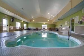 An indoor swimming pool with clear water, surrounded by chairs and a lifeguard chair, with pool rules and exit signs on the walls. - Holiday Inn Express Hotel & Stes Kansas City Sports Complex by IHG (Kansas City)