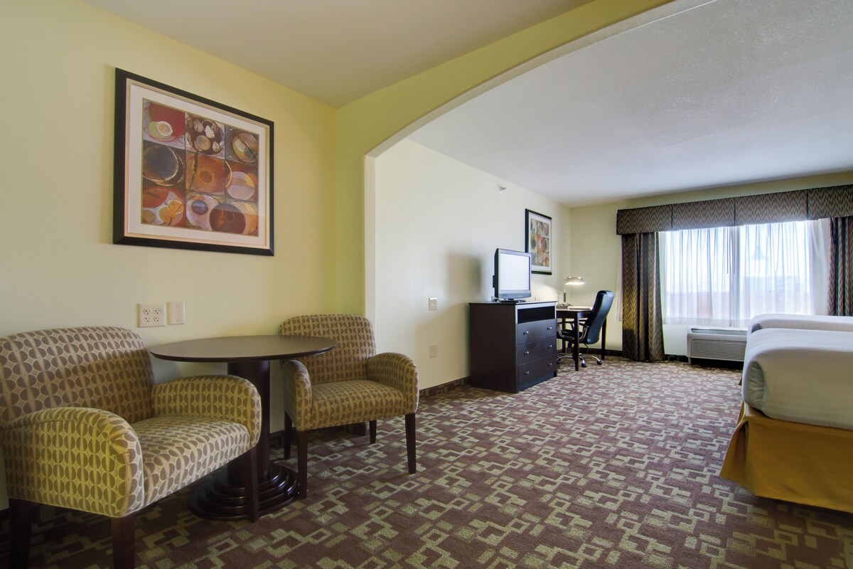 A hotel room with a bed, a desk, two armchairs, a small table, and a television.