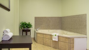 Ein Badezimmer im Eckbereich mit Badewanne, einem kleinen Tisch mit Handtüchern und einem Blumentopf.