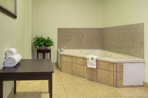 A corner bathroom with a bathtub, a small table with towels, and a potted plant. - Holiday Inn Express Hotel & Stes Kansas City Sports Complex by IHG (Kansas City)